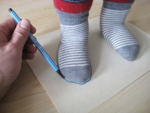 Die Kinderfüße stehen auf einem Blatt Papier und werden mit einem Filzstift umzeichnet